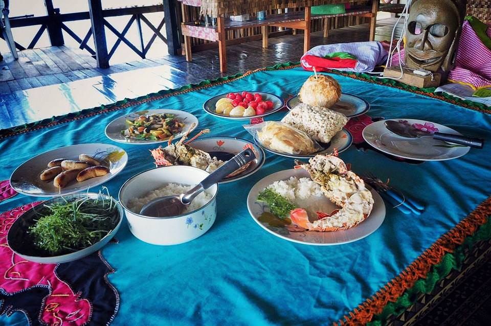 A meal of lobster, rice, greens, sausages and fruit laid out on a bright blue tablecloth